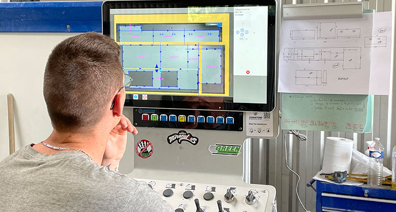 En arbeider foran en CNC-maskin kontrollerer planen for en kjøkkenbenkeplate som er klar for produksjon.